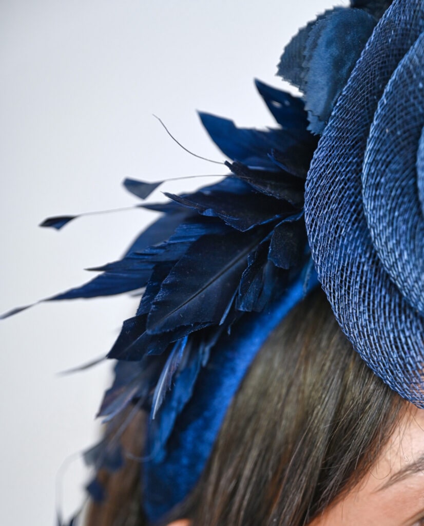 Close-up shot of a navy blue fascinator headpiece by Mizi Atelier featuring mesh and feathers, worn by a woman