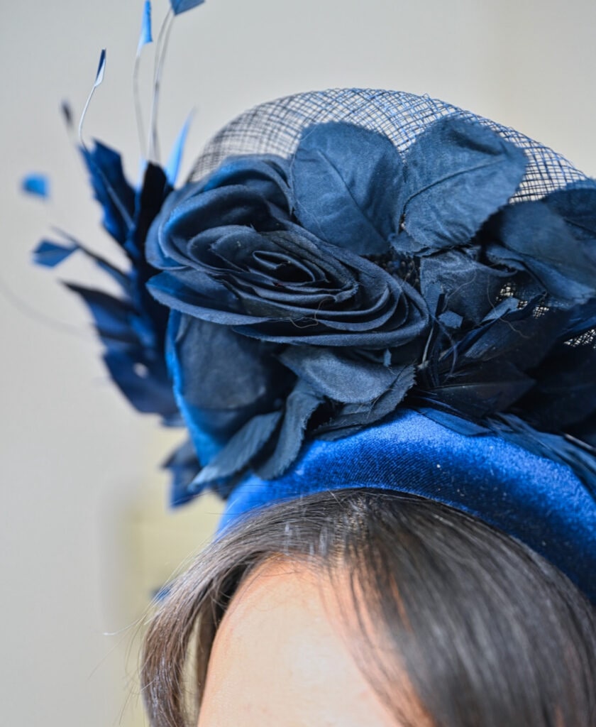 Close-up shot of a navy blue fascinator headpiece by Mizi Atelier featuring a velvet headband, fabric flowers and mesh, worn by a woman