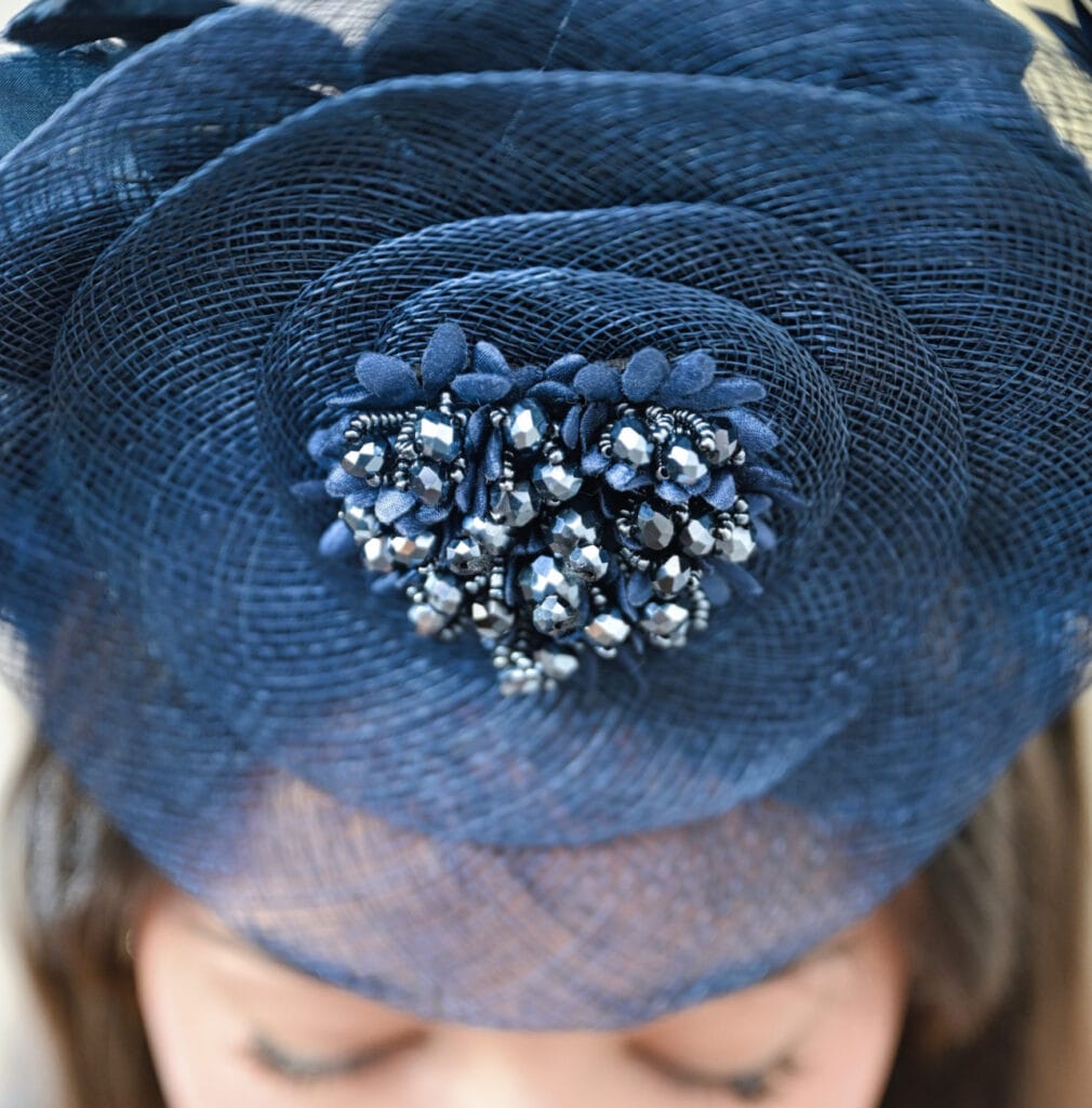 Front-facing close-up shot of a navy blue fascinator headpiece by Mizi Atelier featuring mesh and metallic beads, worn by a woman