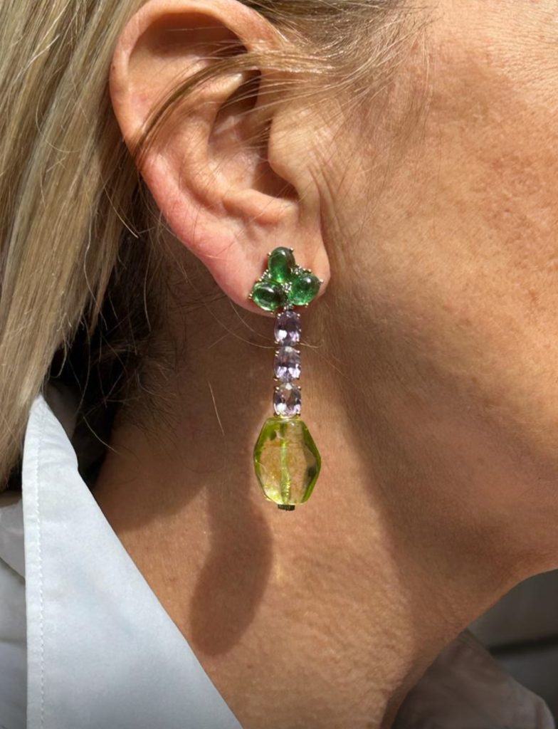 Close-up of a woman wearing long ERA modular earrings by Aurvm Rome featuring green peridot and yellow diamonds.