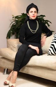 The image features Alessandra the founder of AGpress Sustainable Press Office sat in a off white sofa in black attire and a long pearls necklace.
